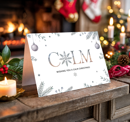 Christmas card with the word "Calm" and festive decorations on a wooden surface with candles and stockings in the background.