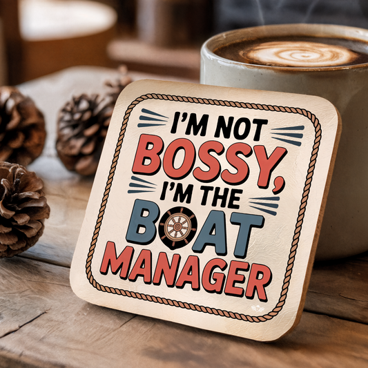Coaster with text "I'm not bossy, I'm the boat manager" on a wooden surface with a coffee cup.