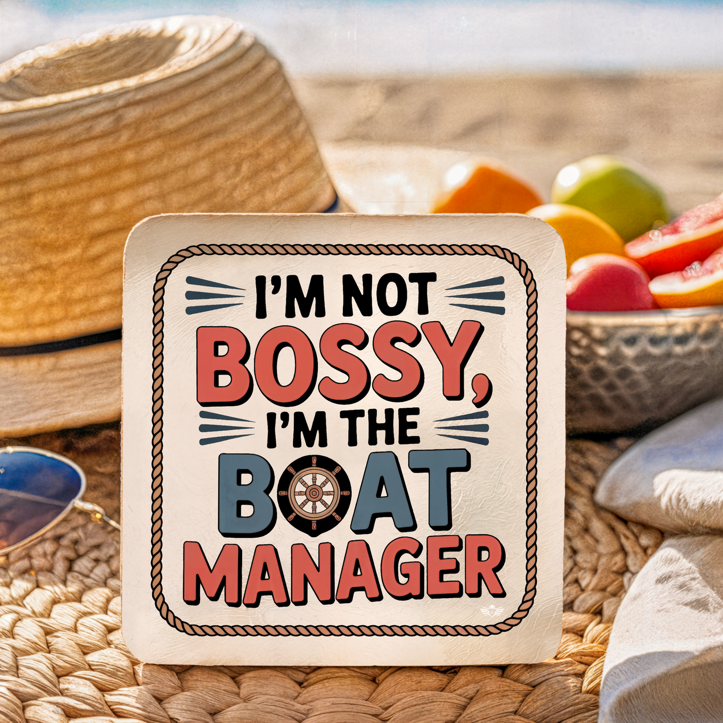 Coaster with "I'm not bossy, I'm the boat manager" text on a woven surface with fruit in the background