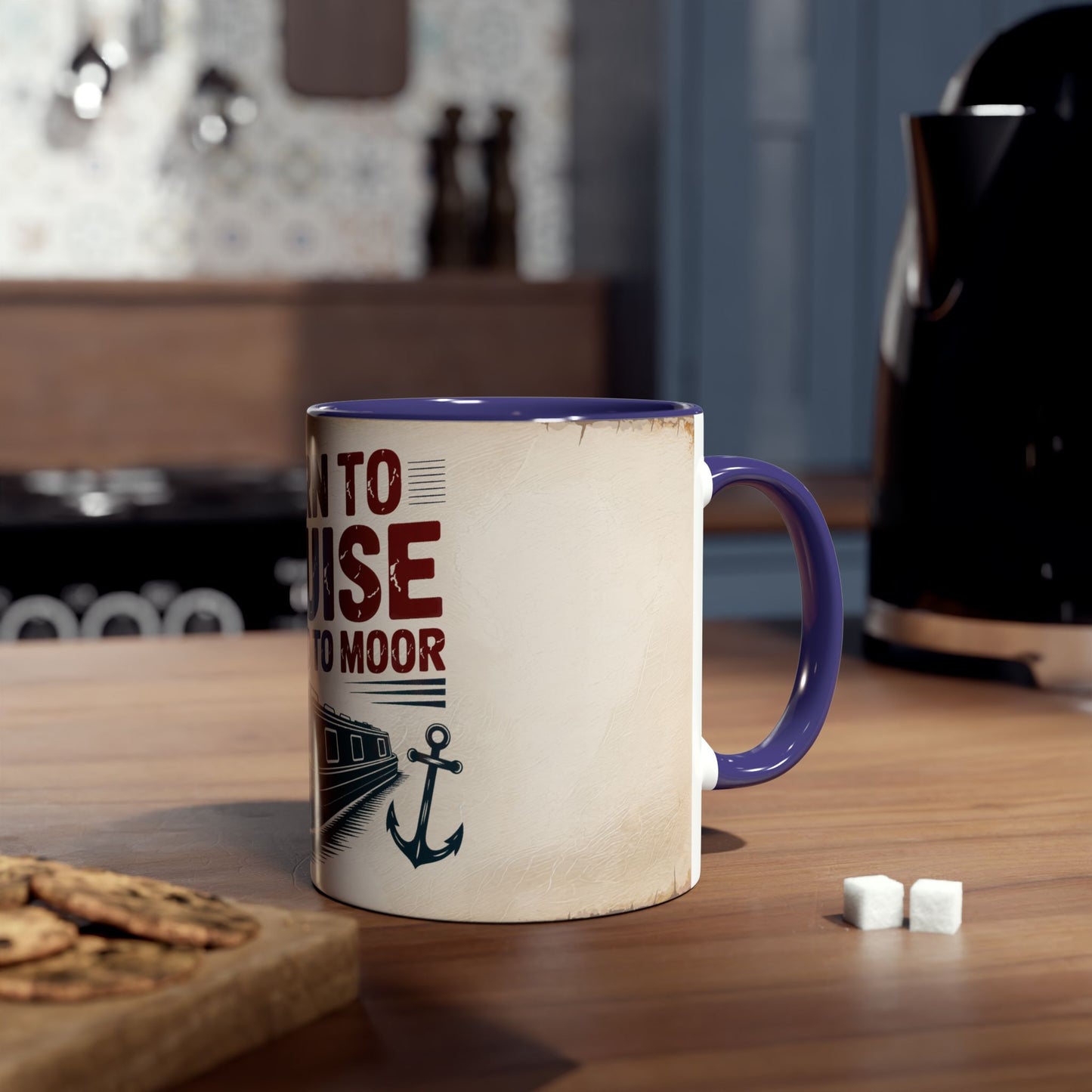 Mug with text and anchor design on a wooden table with cookies and sugar cubes.