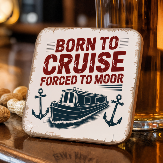 Coaster with "Born to Cruise Forced to Moor" text and boat illustration on a wooden surface.