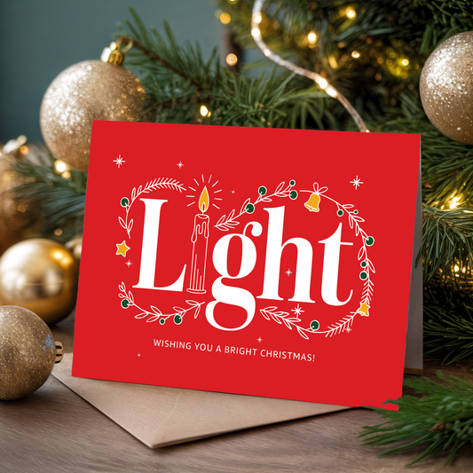 Red Christmas card with "Light" and festive decorations in front of a decorated tree.