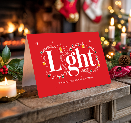 Red Christmas card with "Light" and festive decorations on a wooden surface.