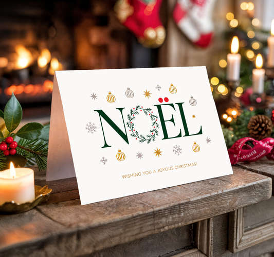 Christmas card with "Noël" and festive decorations on a wooden surface.