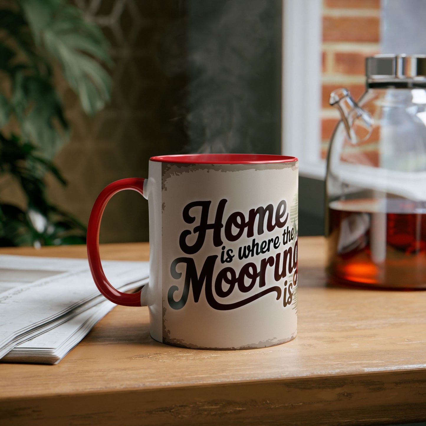 Mug with "Home is where the mooring is" text on a wooden table with newspaper and glass container.