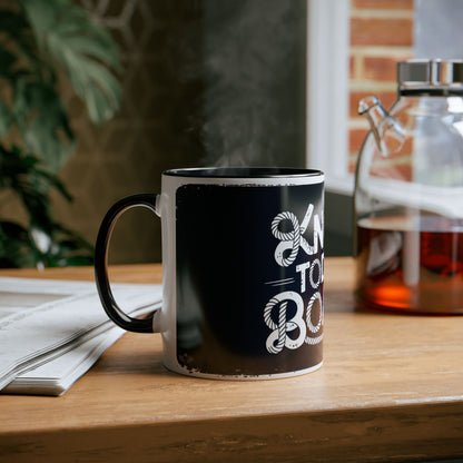 Black mug with white text on a wooden table next to a newspaper and glass container.