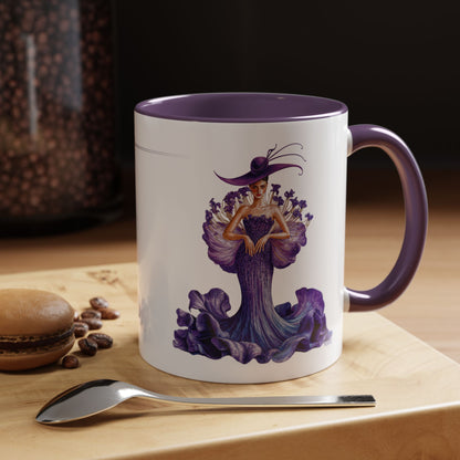 Mug with a decorative design of a woman in a purple dress and hat on a wooden surface with coffee beans and a spoon.